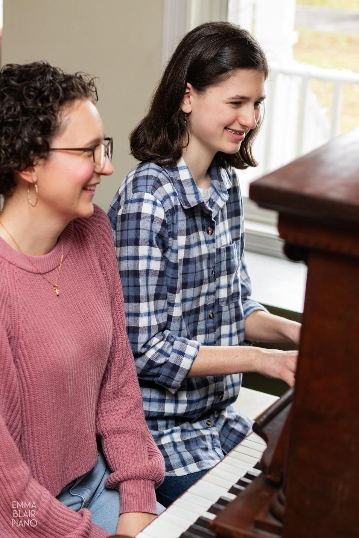 teenage girl playing the piano and smiling beside her piano teacher