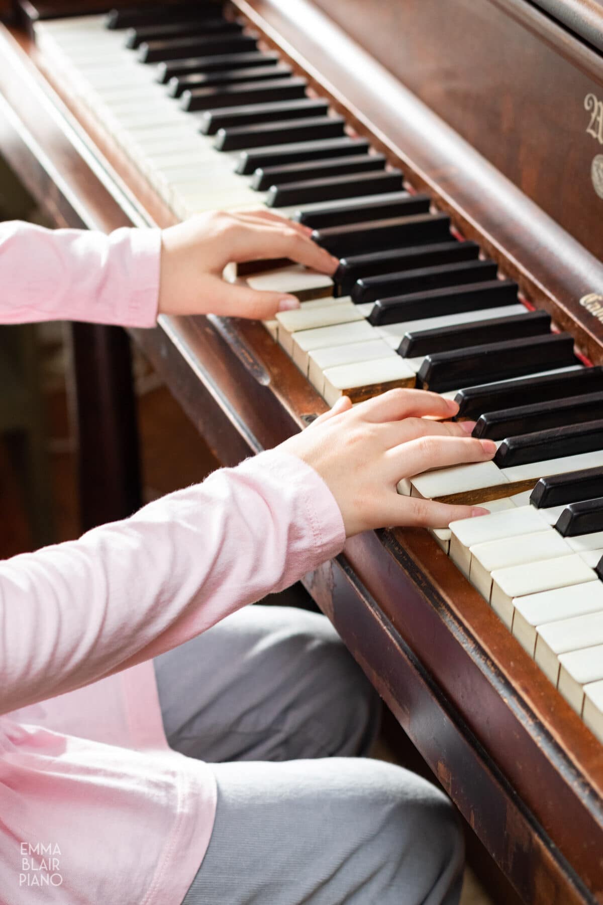 young girl's hands playing an upright piano