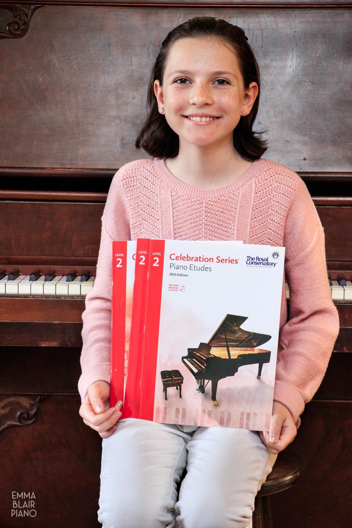 smiling girl holding music books in front of the piano