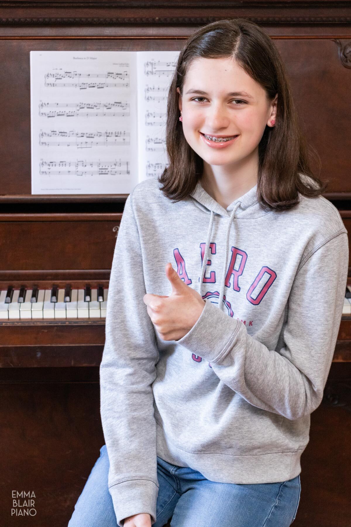 teenage girl smiling and sitting at the piano doing a thumbs up