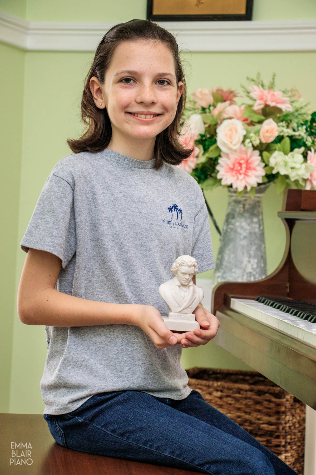 young girl sitting at the piano and holding a small bust of Beethoven