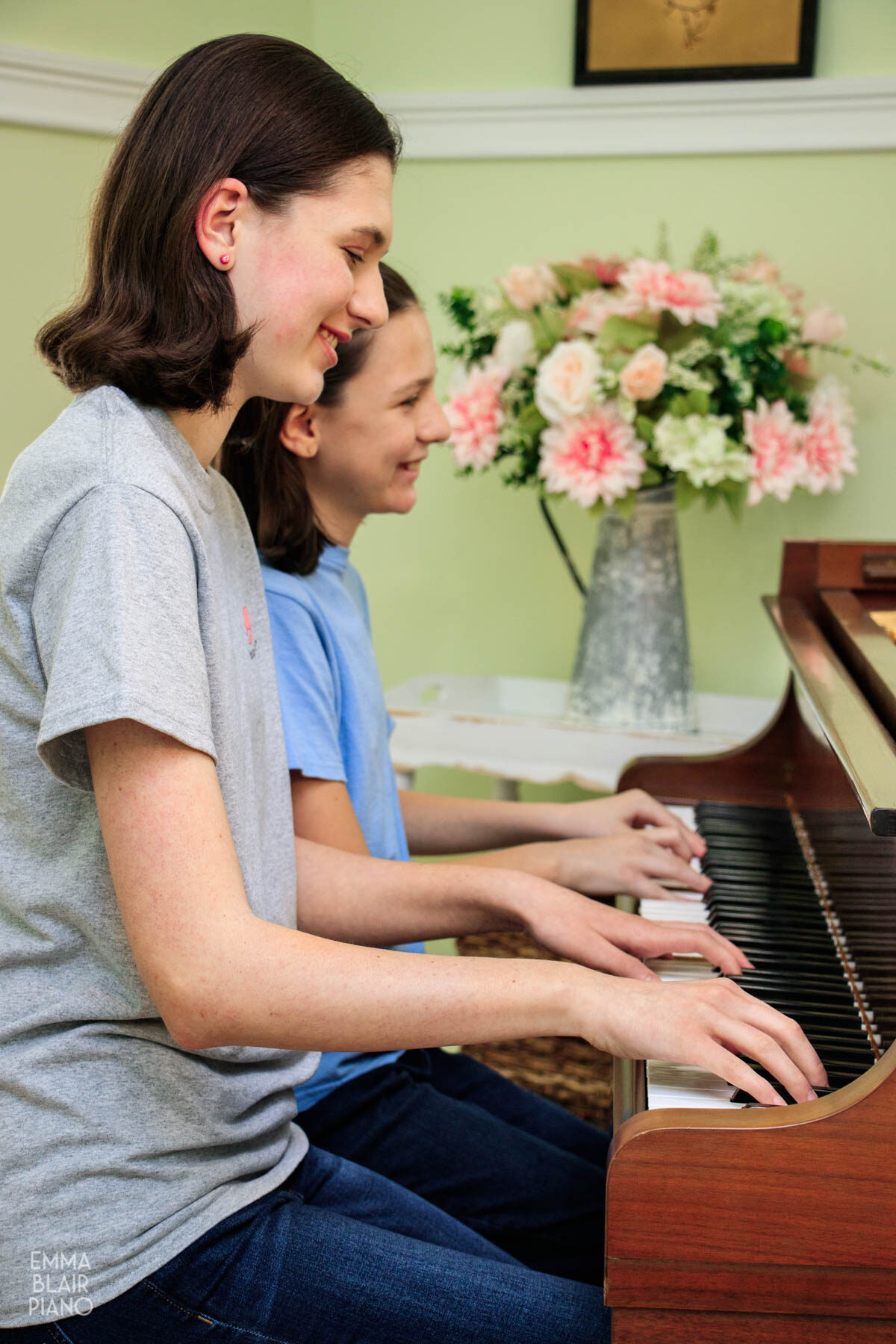 two girls playing a piano duet and smiling