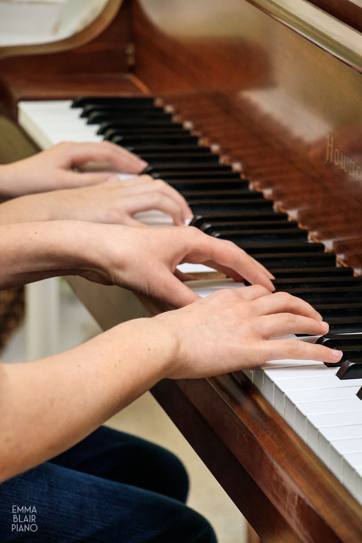 closeup of four hands playing a piano duet