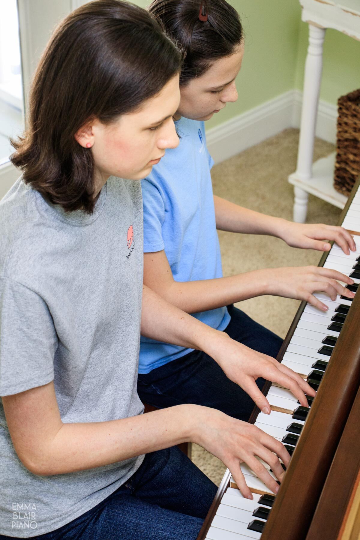 two girls playing a piano duet at a grand piano