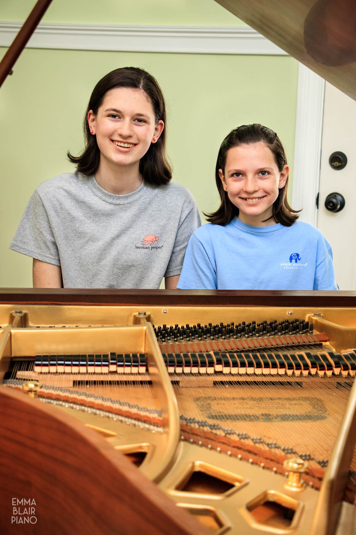 two girls sitting at a grand piano and smiling