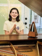 smiling teenage girl clapping a rhythm with a metronome at the piano