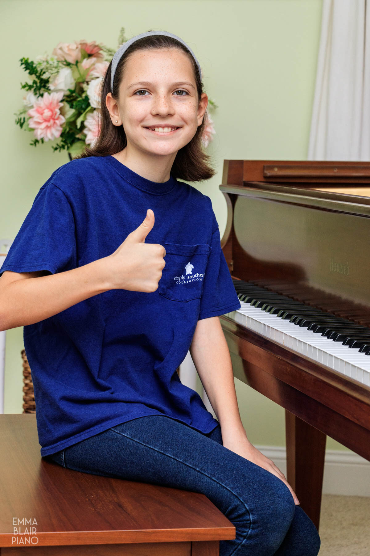 young girl smiling and doing a thumbs up with a piano