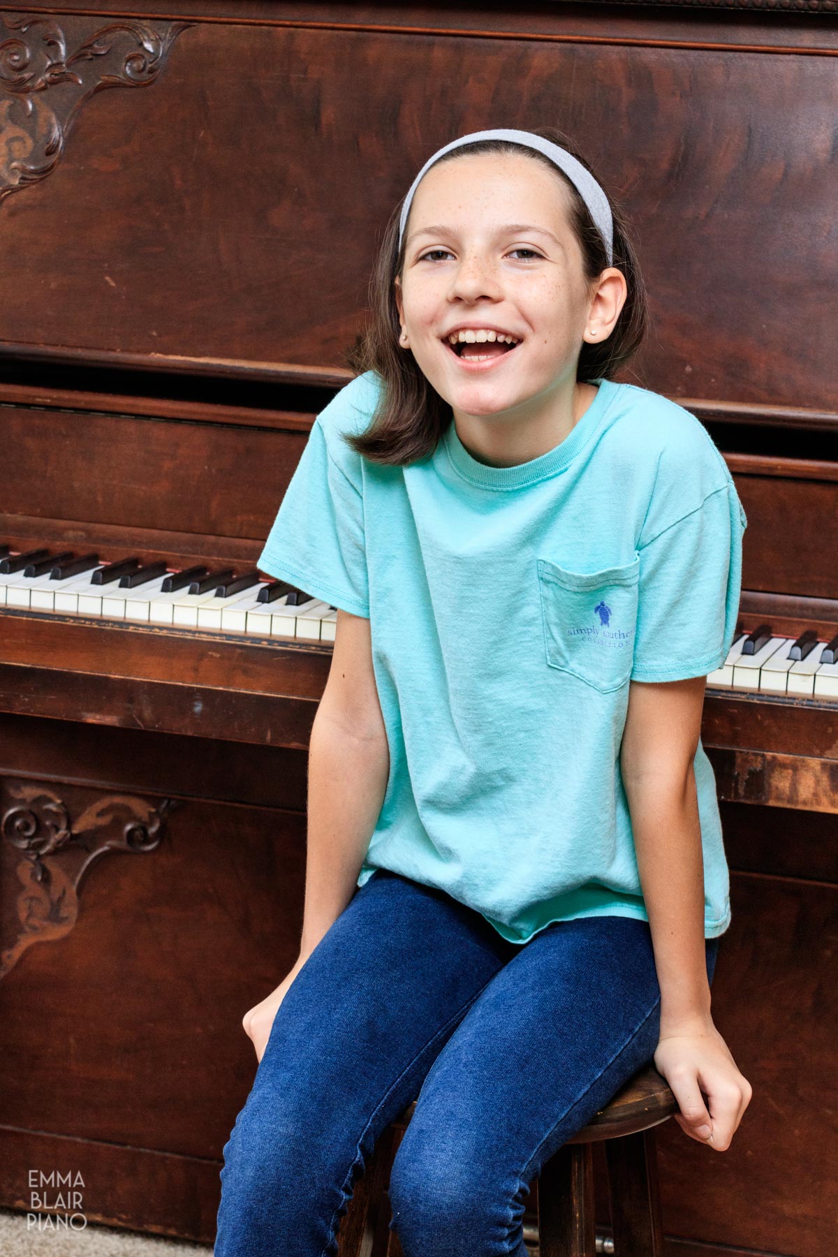 young girl sitting in front of an upright piano and smiling