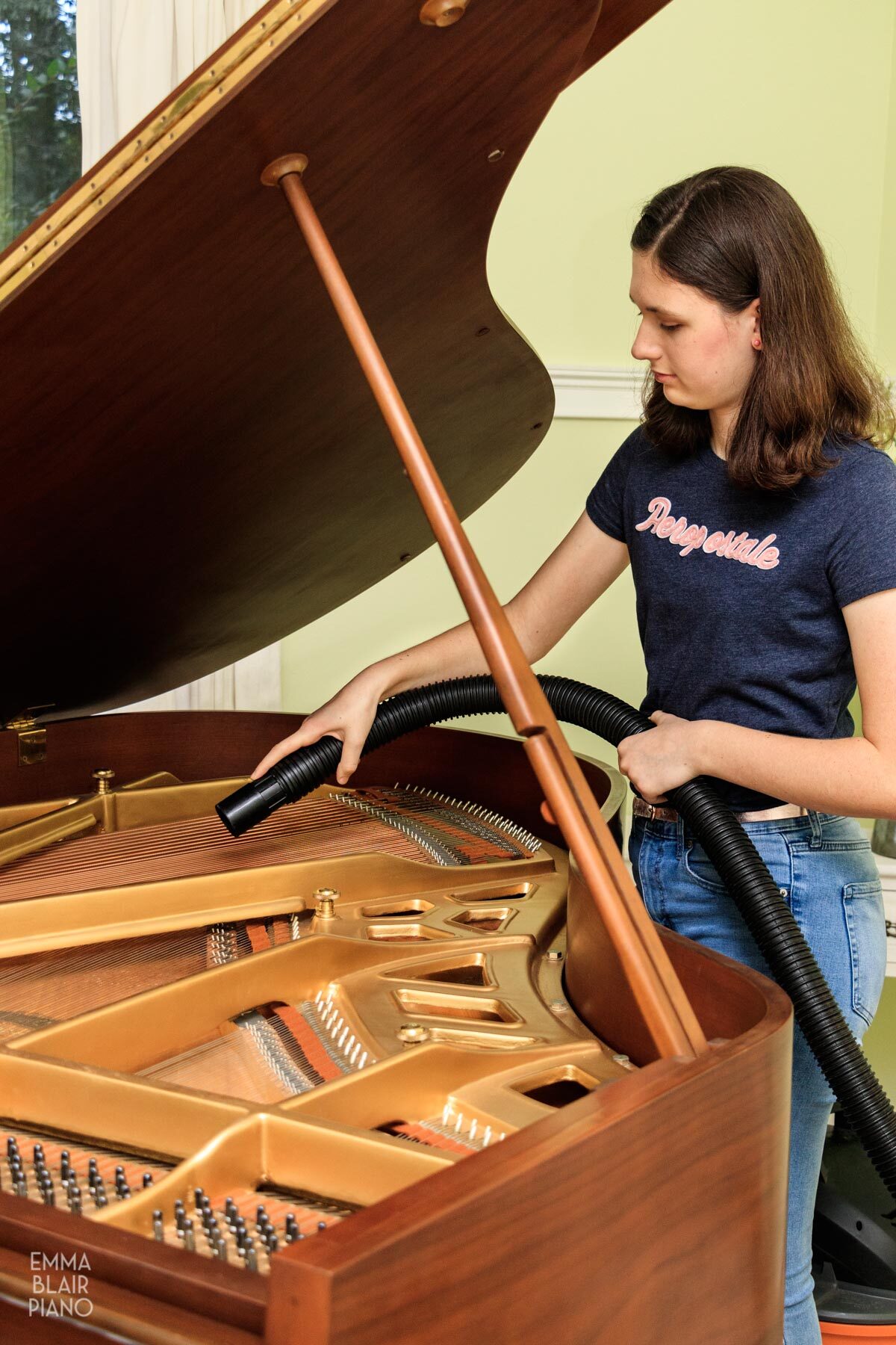 girl blowing dust out of the soundboard of a grand piano